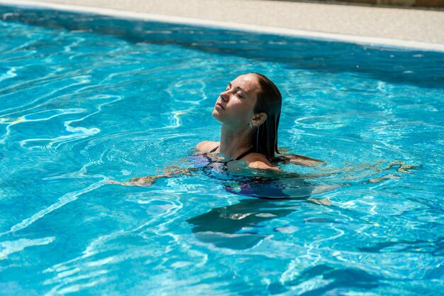 Aantrekkelijke vrouw zwemt uit het water in helder zwembad Spa en ontspanning