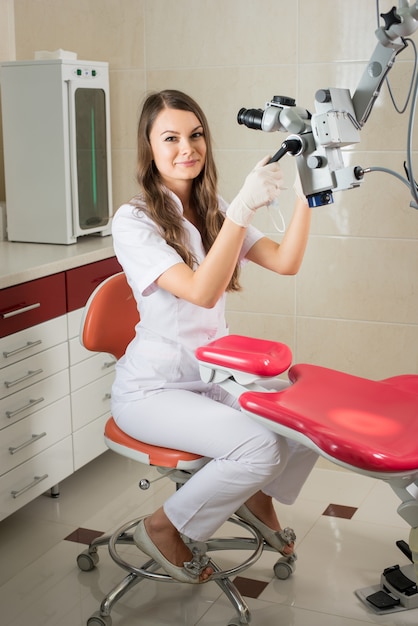 Aantrekkelijke vrouwelijke arts in handschoenen met microscoop op het werk in het moderne tandartsbureau.