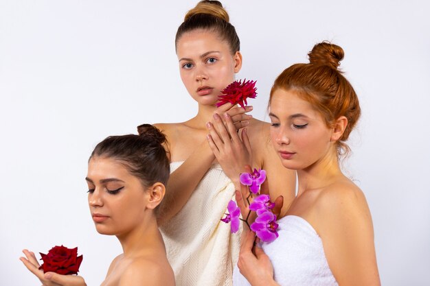 Aantrekkelijke vrouwelijke modellen met haar naar achteren getrokken, gewikkeld in witte handdoeken en met bloemen. Poseren op een witte muur. Hoge kwaliteit foto