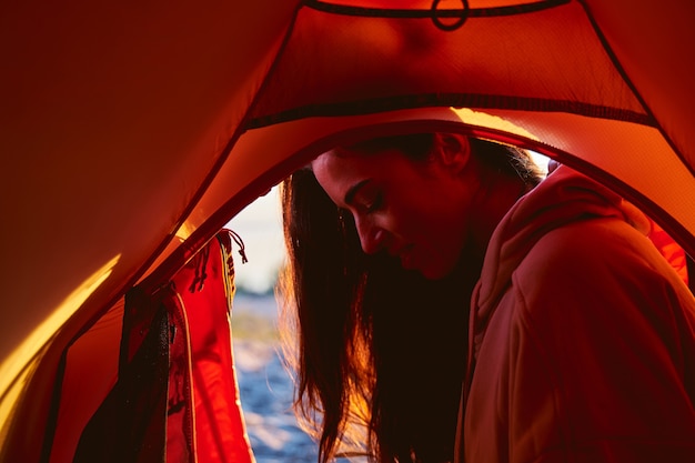 Foto aantrekkelijke vrouwelijke reiziger die naar beneden kijkt en glimlacht terwijl hij in de buurt van een toeristische tent rust