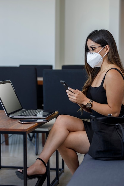 Aantrekkelijke vrouwelijke zakenvrouw met masker die vanuit huis op haar computer werkt om berichten te verzenden