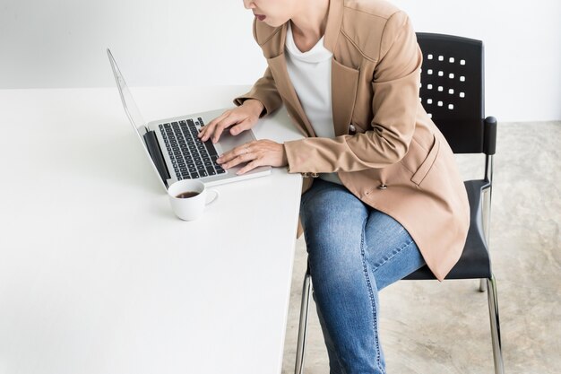 Aantrekkelijke vrouwen in casual business zitten aan een tafel werken op haar laptop computer thuis kantoor voor een raam.