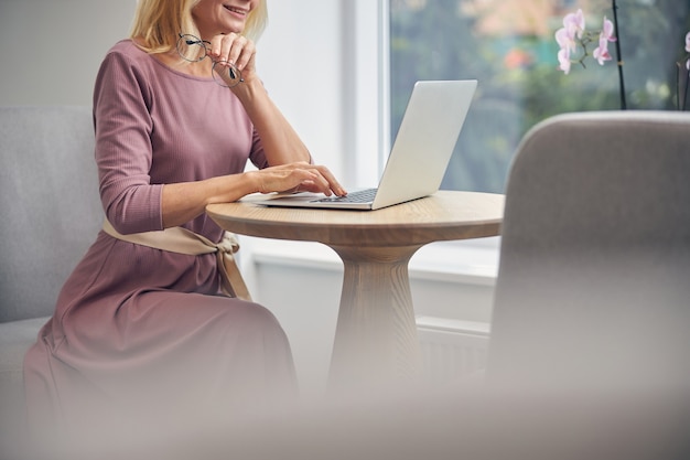 Aantrekkelijke zakenvrouw die glimlach op haar gezicht houdt terwijl ze naar het scherm van haar laptop kijkt