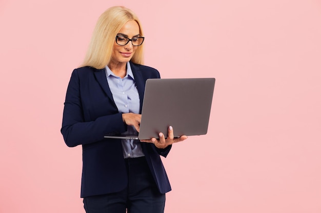 Aantrekkelijke zakenvrouw van middelbare leeftijd in een bril met een laptop op een roze achtergrond