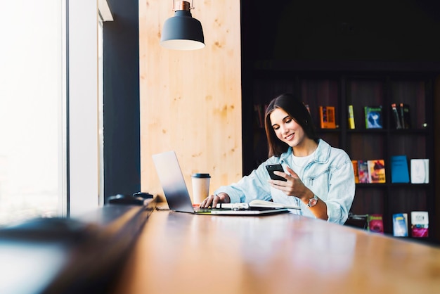 Aantrekkelijke zakenvrouw zit aan tafel voor laptop en praat over de mobiele telefoon, onderhandelt over de telefoon.