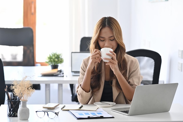 Aantrekkelijke zakenvrouw zittend op haar werkplek koffie drinken in de ochtend.