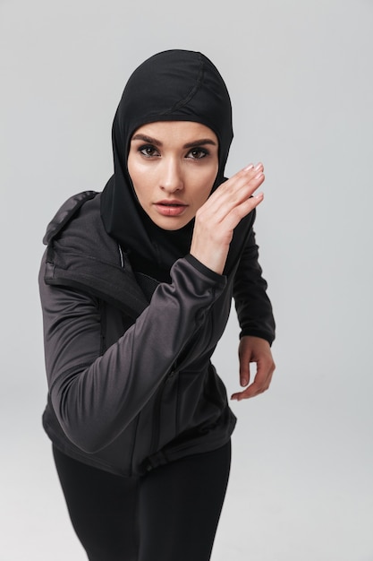Aantrekkelijke zelfverzekerde jonge moslimvrouw die een sport-hijab draagt die geïsoleerd loopt