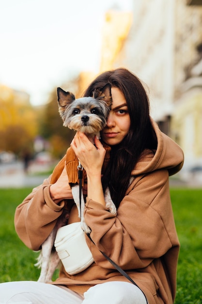 aantrekkelijke zelfverzekerde jonge vrouw die haar schattige kleine yorkshire terrier vasthoudt