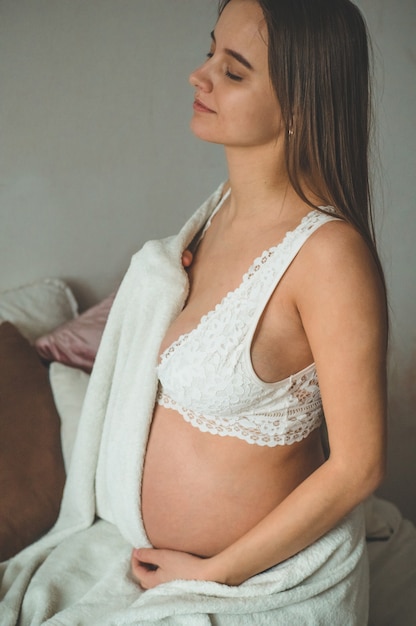 Aantrekkelijke zwangere vrouw zit in bed en houdt haar buik. laatste maanden zwangerschap.