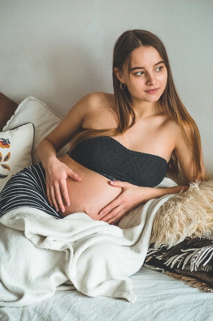 Aantrekkelijke zwangere vrouw zit in bed en houdt haar buik. Laatste maanden zwangerschap.