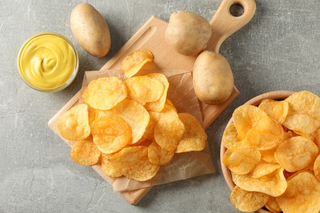 Aardappelchips. Biersnacks, saus, aardappel op snijplank, op grijs, ruimte voor tekst. Bovenaanzicht