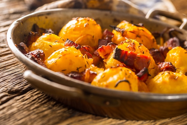 Aardappelen. Geroosterde aardappelen met spekui en worstjes op oude eiken tafel.