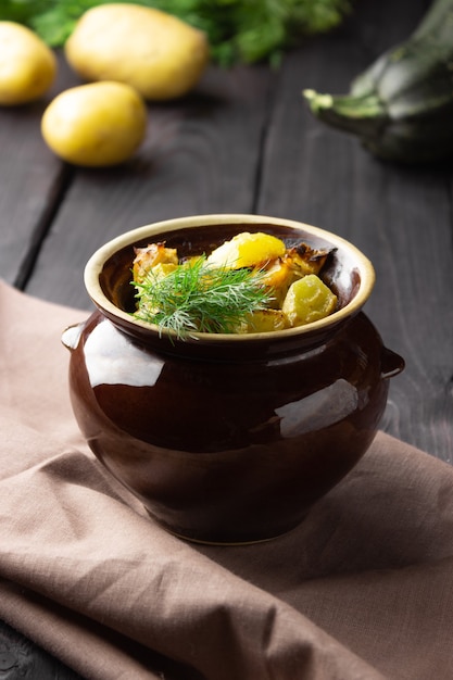 Foto aardappelen, kip en courgette gebakken in een aarden pot op een donkere achtergrond.