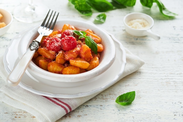 Aardappelgnocchi Traditionele huisgemaakte aardappelgnocchi met tomatensaus, basilicum en parmezaanse kaas op keukentafel op lichtgrijze keukentafelachtergrond Traditioneel Italiaans eten Bovenaanzicht