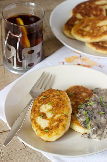 Aardappelkoteletten of pannenkoeken met champignonsaus en groene uien. Rustieke stijl.