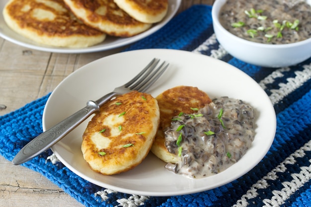 Aardappelkoteletten of pannenkoeken met champignonsaus en groene uien. Rustieke stijl.