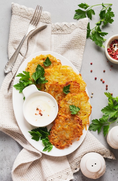 Aardappelpannenkoekjes met zure room, kruiden en knoflook in witte ceramische plaat op grijze oude concrete lijst.