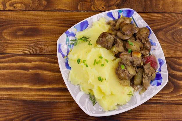 Aardappelpuree met gestoofde kippenlever met appel en ui op houten tafel