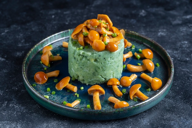 Aardappelpuree met groene spirulina en honingpaddestoelen in een bord, close-up