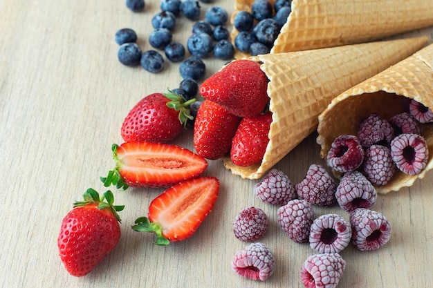 Foto aardbei bosbes framboos in wafel kegels op lichte houten achtergrond close up