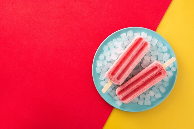 Aardbei ijslollys met ijs op geel en rood oppervlak