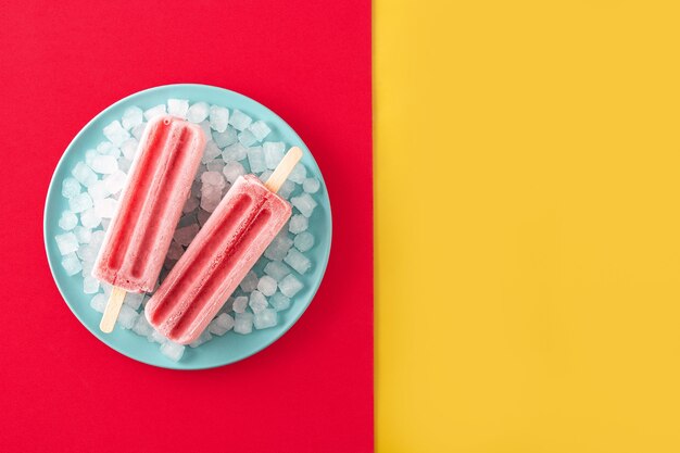 Aardbei ijslollys met ijs op geel en rood oppervlak