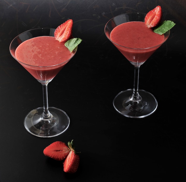 Aardbei smoothie in cocktailglas met aardbei en munt op zwarte