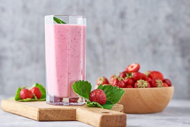 Aardbei smoothie in glazen pot en verse aardbeien in houten kom op een snijplank