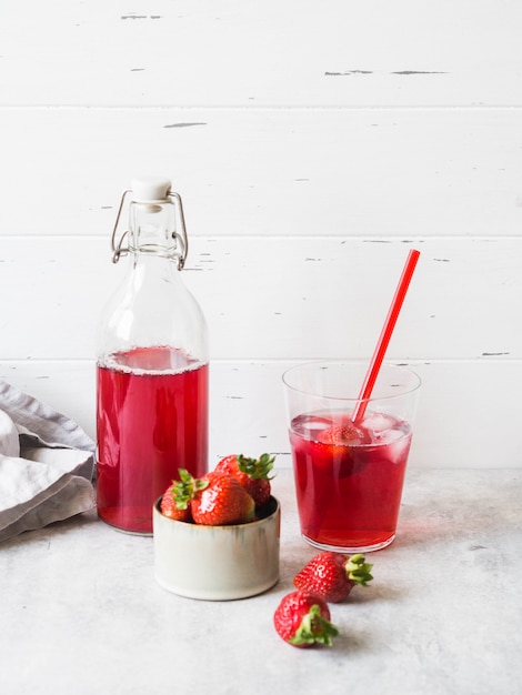 Aardbeidrank in een glazen fles. Koele bessencompote in een fles en glas met rietje