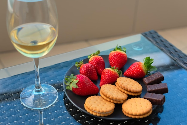 Aardbeien en snoep op bord close-up met selectieve focus met glas champagne of witte wijn op een tafel op balkon of terras Luxe levensstijl romantiek concept