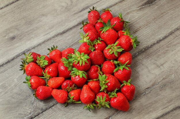 Aardbeien gerangschikt in de vorm van een hart, geplaatst op een grijs houten bureau.