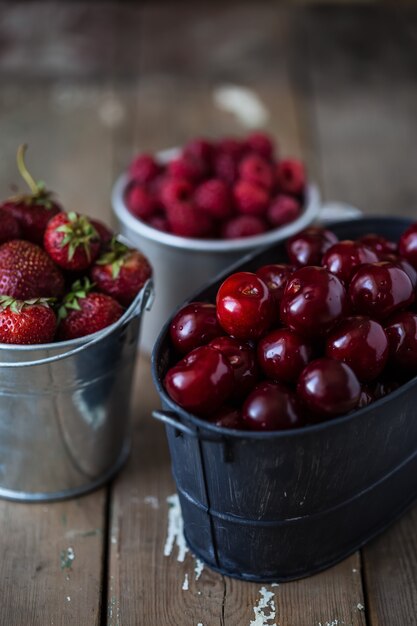 Aardbeien, kersen, frambozen in emmers op een houten tafel