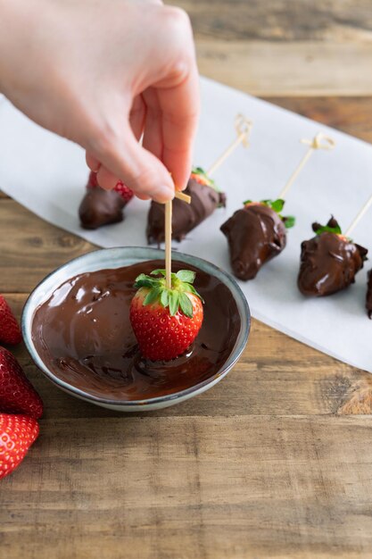 Aardbeien met chocolade op een houten achtergrond Hand dompelen een aardbei in de kom met chocolade Verticale foto