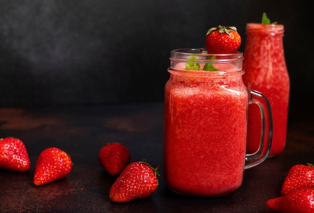 Aardbeien smoothies of aardbeien met ijs in een pot. Een verfrissend zomerdrankje. Zwarte achtergrond. Vooraanzicht. Kopieer ruimte