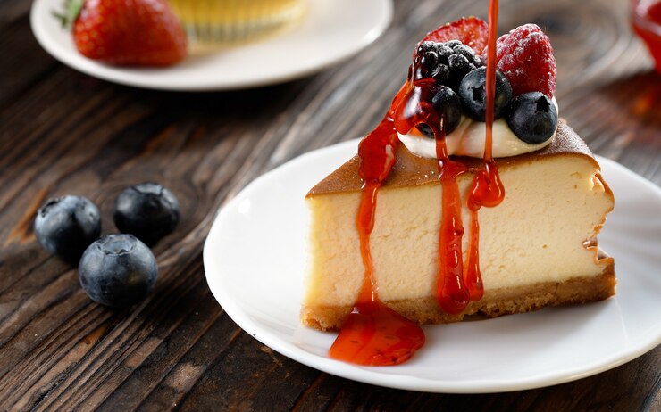 Foto aardbeien topping gieten op vers plakje cheesecake met bosbessen zoet en natuurlijk product lekker gebakken dessert op houten achtergrond handgemaakt gebak voorgerecht bakkerijproduct in slow motion