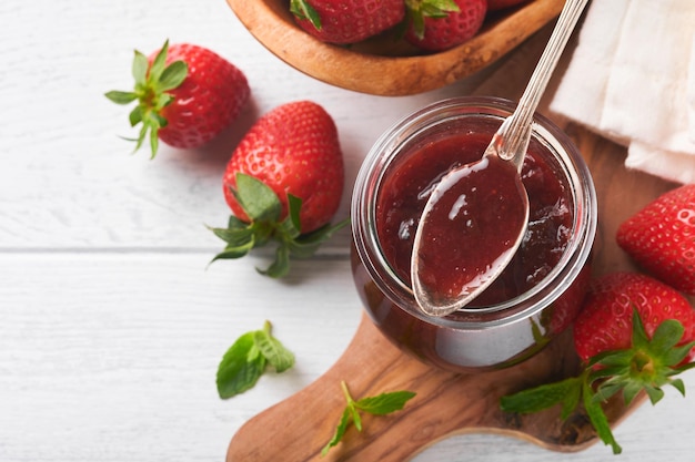 Aardbeienjam Aardbeienjam in glazen pot met verse bessen plaat op witte houten tafel achtergrond close-up zelfgemaakte aardbeien fruitige jam bovenaanzicht met kopie ruimte