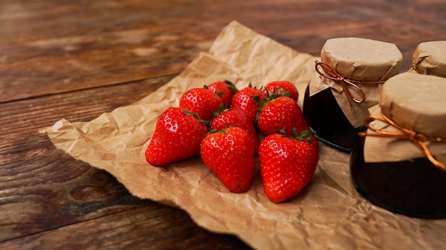 Aardbeienjam in de glazen pot met verse bessen op houten achtergrond