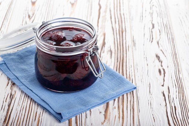 Aardbeienjam in glazen pot met blauw servet op witte houten tafel Zelfgemaakte geconserveerde vruchten