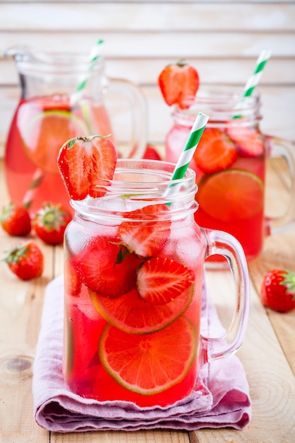 Aardbeienlimonade met limoen en ijs in glazen pot op een houten tafel