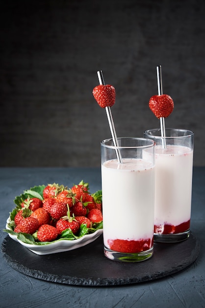 Aardbeienmelk smoothie in glas met stro en verse bessen op donkere achtergrond