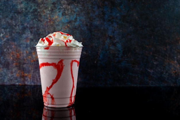 Aardbeienmilkshake met aardbeiensiroop in helder glas op donkere achtergrond