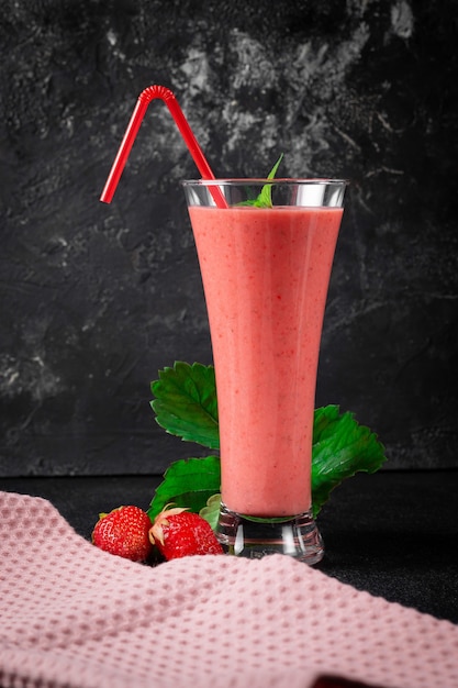 Aardbeienmilkshake met pepermunt in een glas op een donkere stenen muur. gezond eten voor ontbijt en snacks.