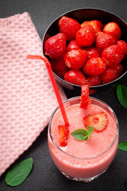 Aardbeienmilkshake met pepermunt in een glas op een donkere stenen ondergrond. Gezond eten voor ontbijt en snacks.