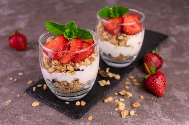 Aardbeienparfait in een glas met yoghurt en muesli op een grijze achtergrond