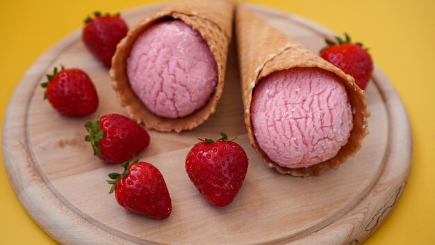 Aardbeienroomijs in een wafelkegel. IJs en bessen op een gele zomerachtergrond