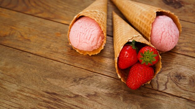 Aardbeienroomijs in een wafelkegel. Rode bessen en ijsballen op een houten ondergrond.