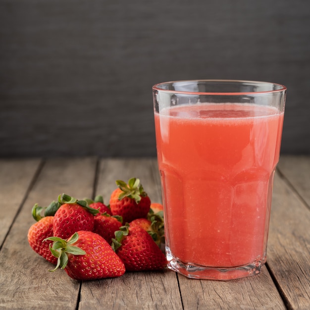 Aardbeiensap in een glas met fruit over houten tafel.