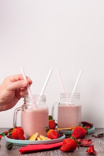 aardbeiensmoothies en koekjes in potjes op turquoise borden met stukjes biscuit en wat aardbeien rond de potjes