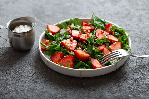 Aardbeisalade met rucola op een bord met een vork op lichtgrijze achtergrond