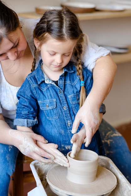 Aardewerkworkshop handgemaakte ambachtelijke ambachtsman leert een kindmeisje hoe ze klei op een pottenbakkersschijf moet vormen en vormen